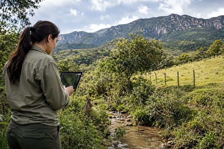 Técnica avaliando área de preservação e nascente com tablet para regularização ambiental